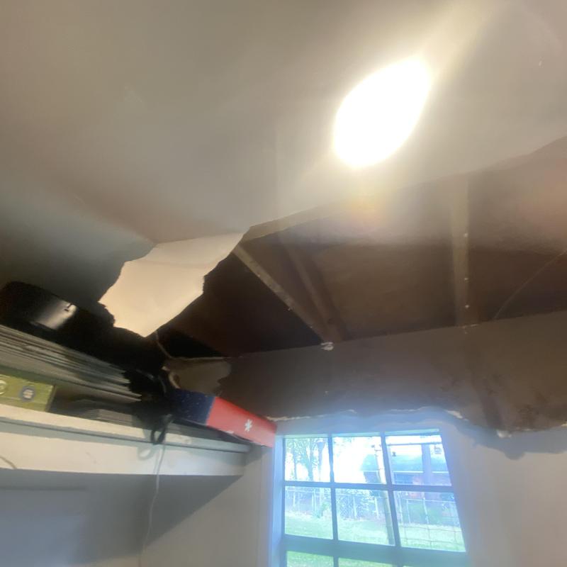 Ceiling drywall with large water damage hole and exposed wood beams