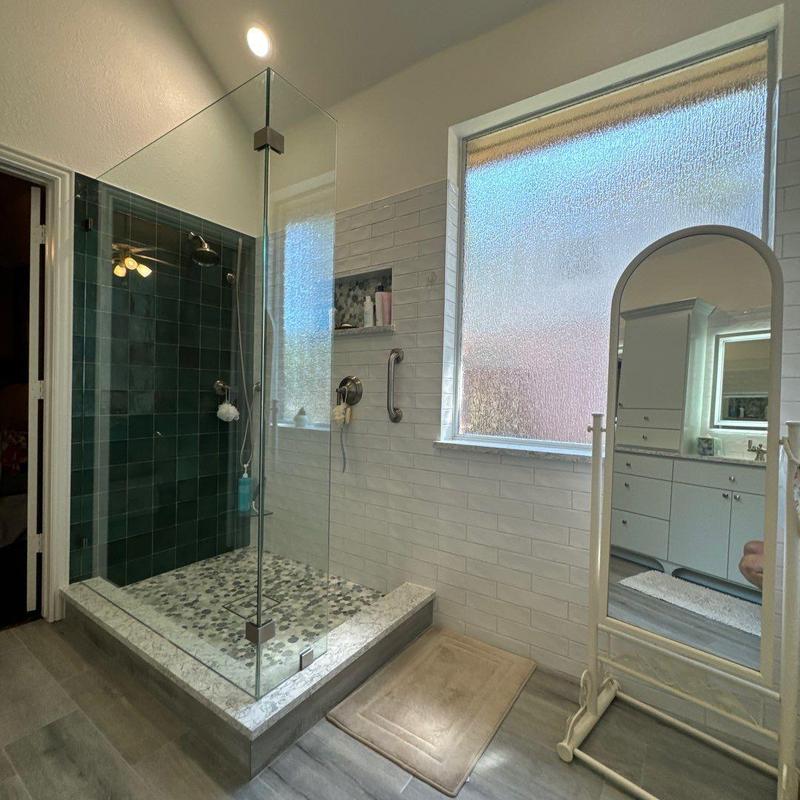 Glass shower enclosure with pebble tile floor and grab bar