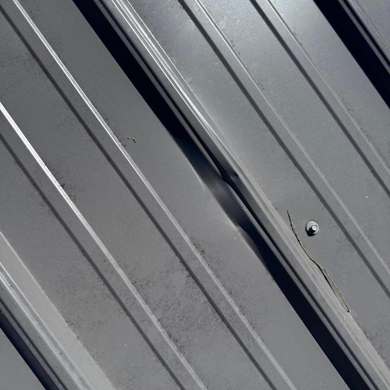 Metal roof panel dent and crack near fastener