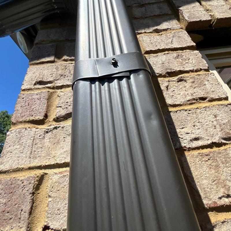 Metal downspout with dent near mounting bracket on brick wall