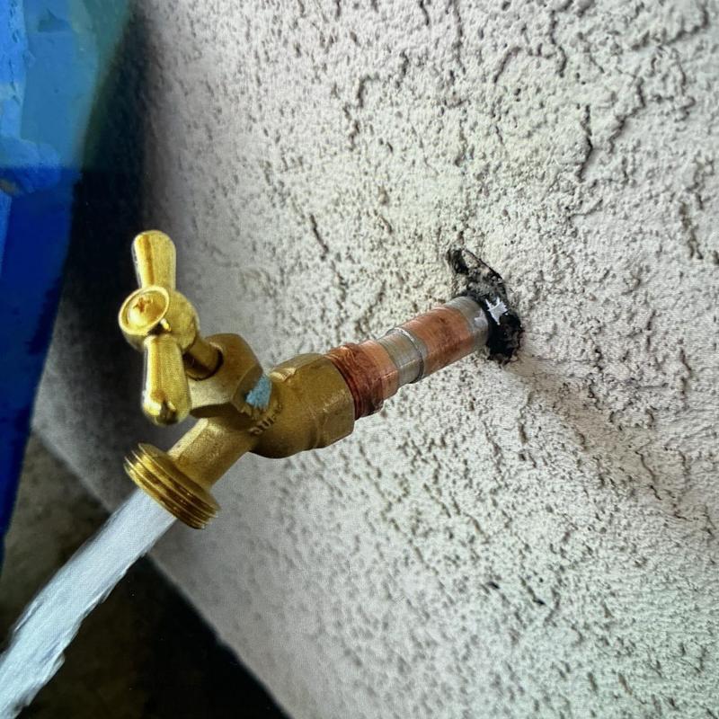 Brass hose bib with water flowing from wall-mounted pipe