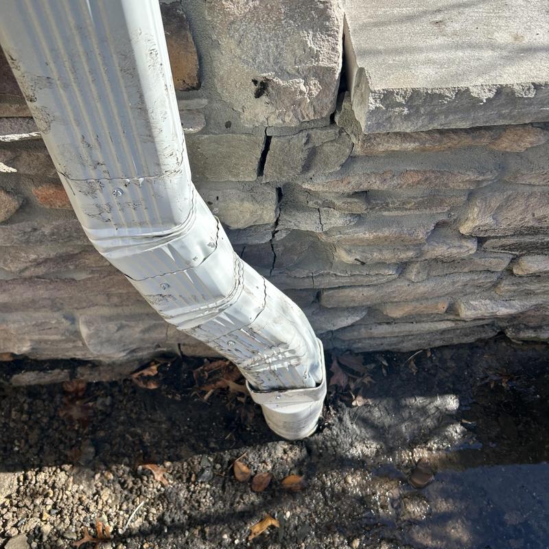 Downspout with leaking joint near cracked stone wall Downspout with leaking joint near cracked stone wall