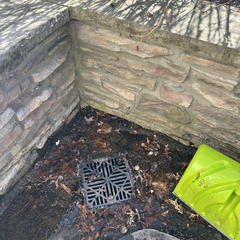 Outdoor drain grate surrounded by leaves and stone wall Outdoor drain grate surrounded by leaves and stone wall