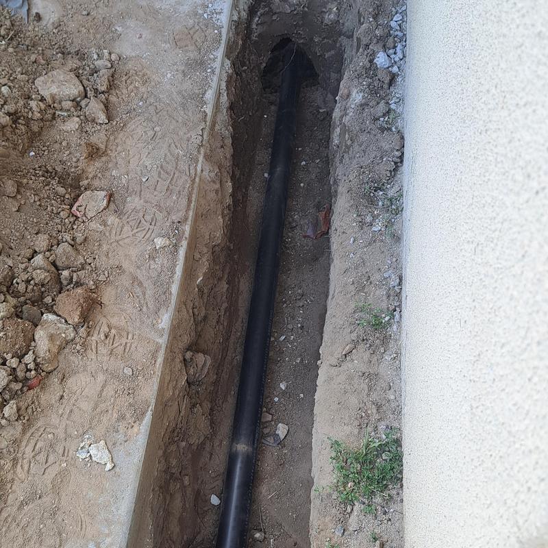 Sewer cleanout pipe installed in trench beside wall