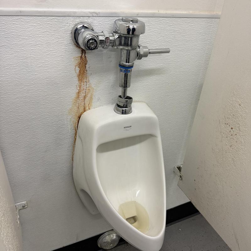 Urinal flushometer valve with rust stains on wall