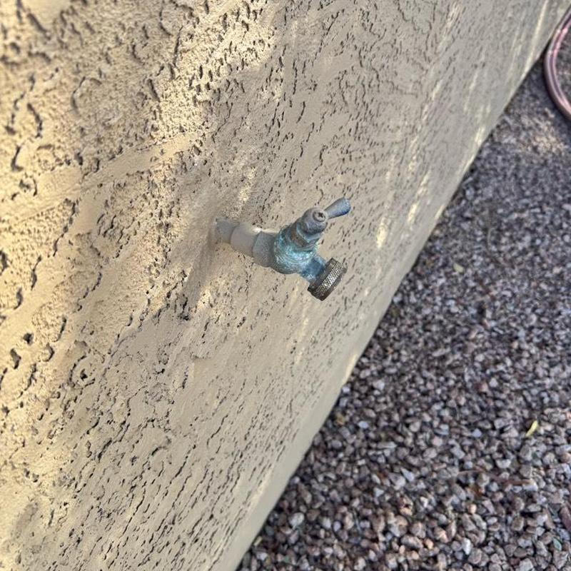 Outdoor hose bib faucet on stucco wall with gravel ground