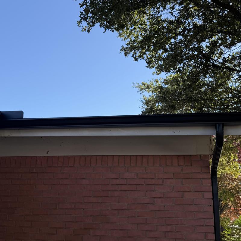 Black gutter system installation on brick house roofline