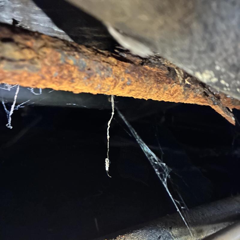Rusty gas leak pipe with cobwebs under home