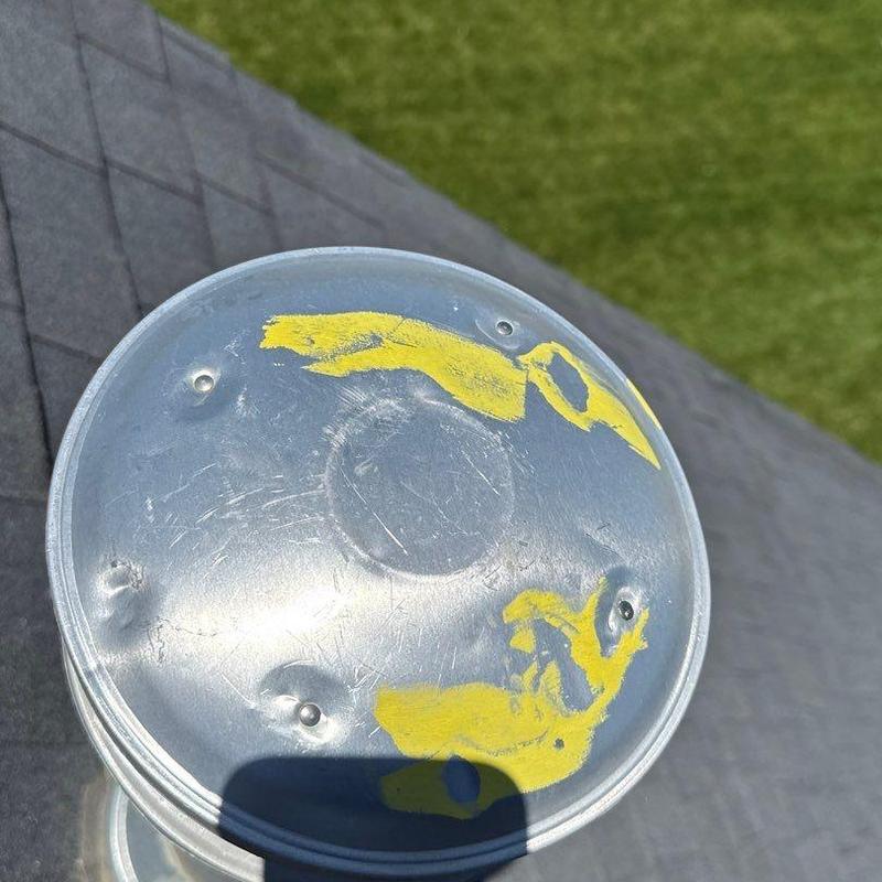 Metal vent cap with hail dents and yellow markings