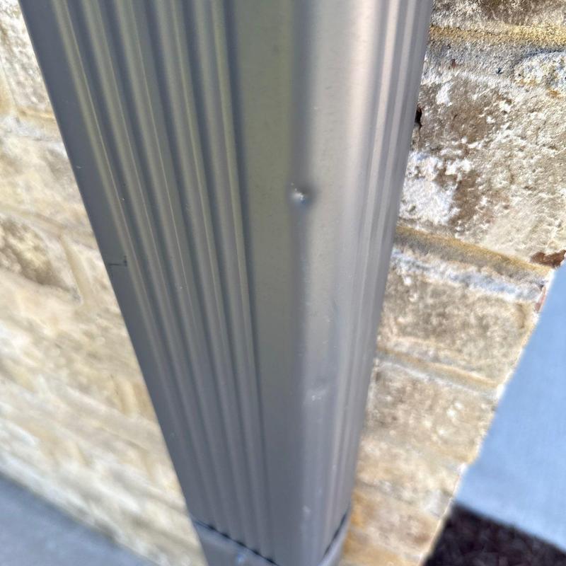 Metal downspout with hail dent against brick wall