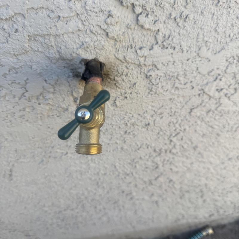 Hose bib with green handle installed on exterior wall