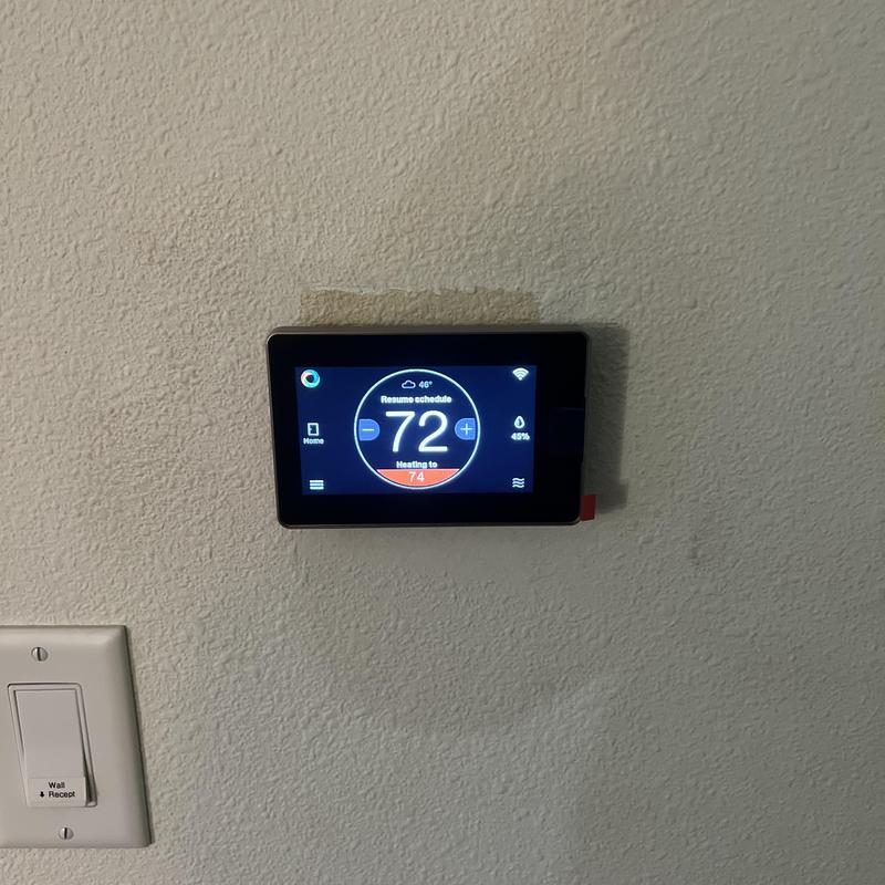 Smart thermostat displaying heating set to 74°F on wall Smart thermostat displaying heating set to 74°F on wall