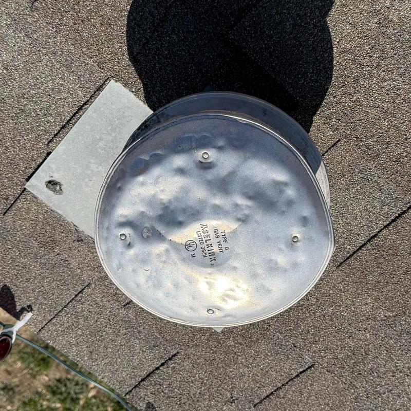 Metal gas vent cap with impact dents on roof shingles