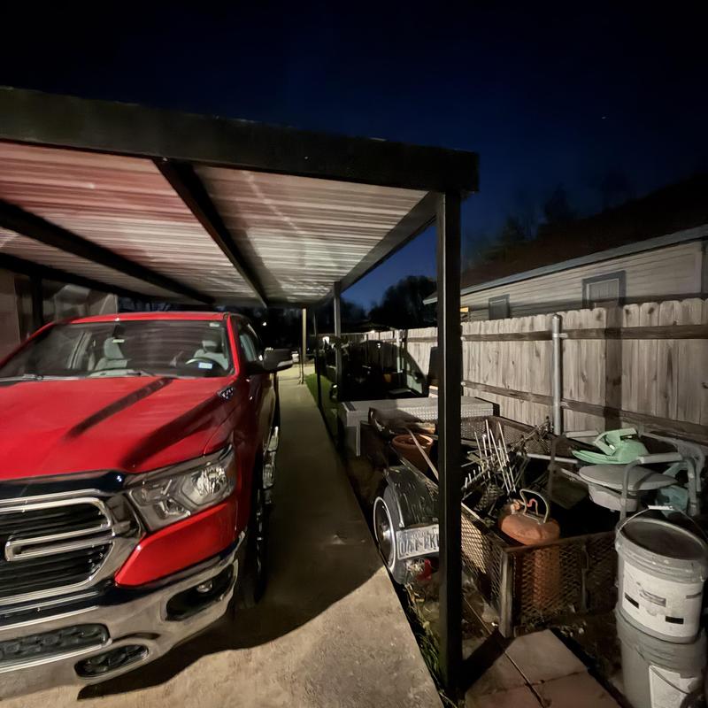 Metal carport with red truck parked underneath at night