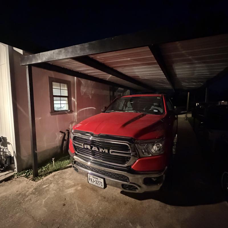 Metal carport covering red RAM truck at night