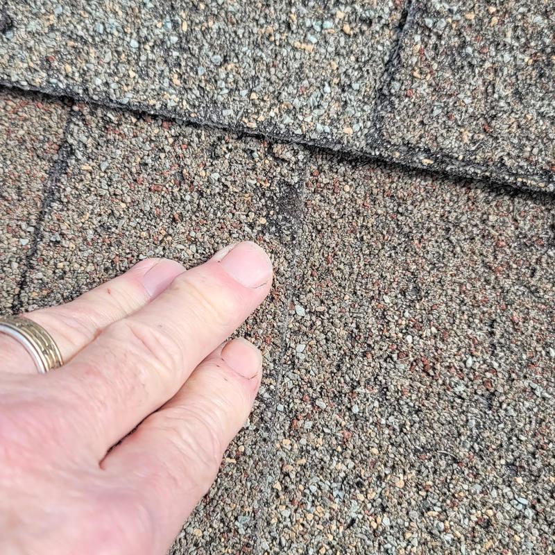 Roof shingles showing hail damage close-up with hand