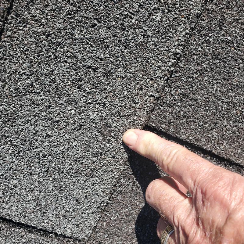 Asphalt roof shingle with wind and hail damage close-up