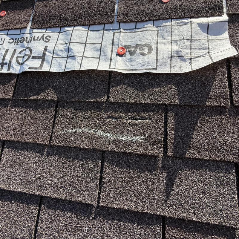 Roof shingles with visible damage and roofing underlayment