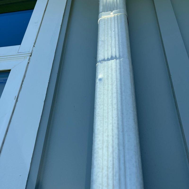 Metal downspout with hail damage dent near bracket