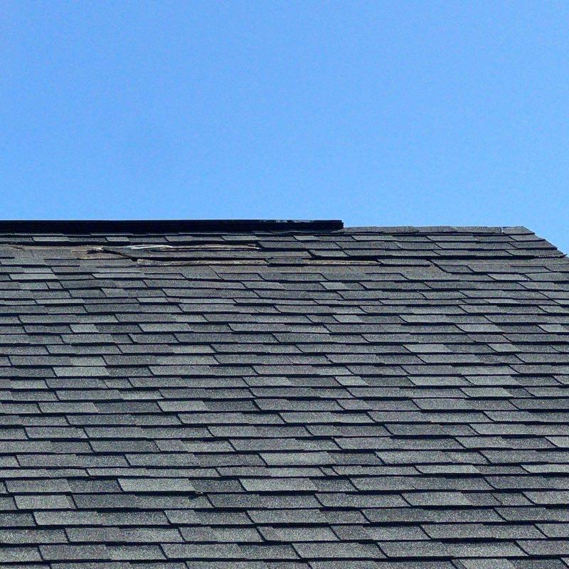 Worn asphalt shingles on residential roof under clear sky