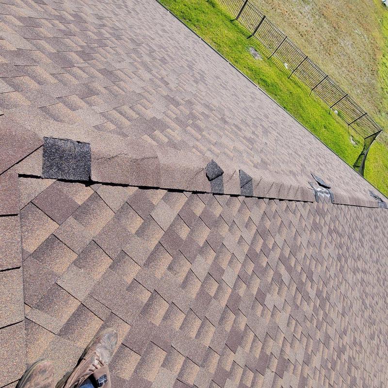 Shingle ridge with damaged and lifted shingles on roof