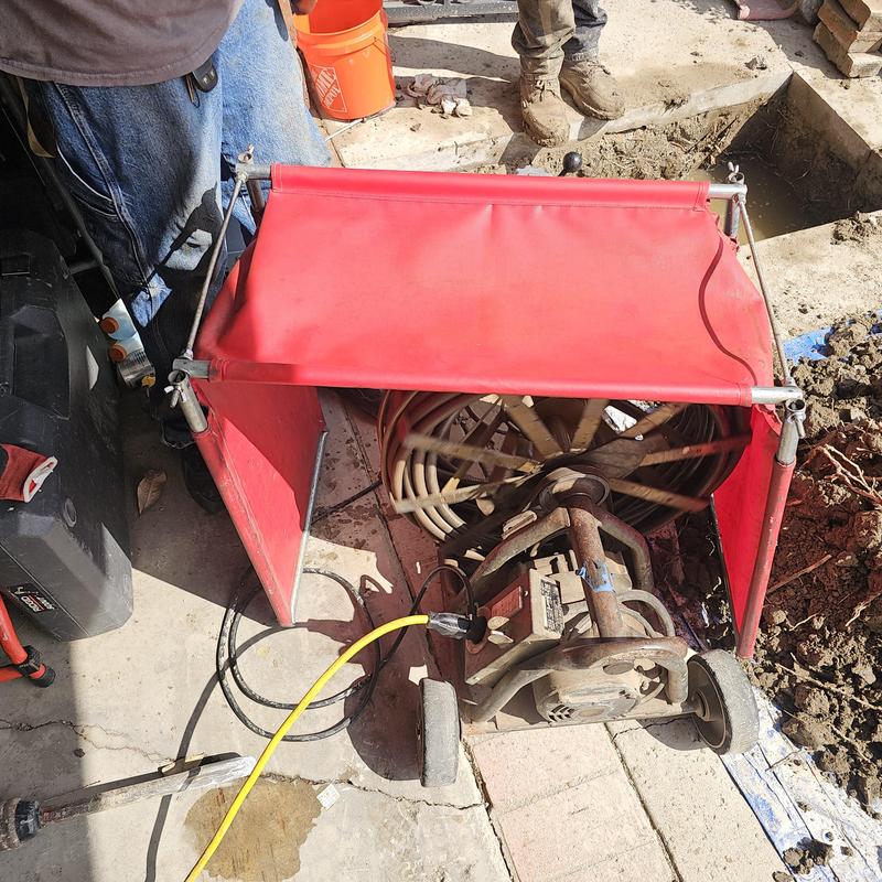Sewer snake machine with red splash guard on driveway
