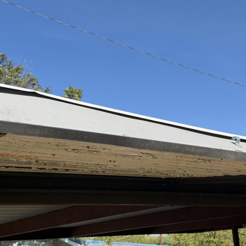 Metal carport roof edge with bent panels under clear sky