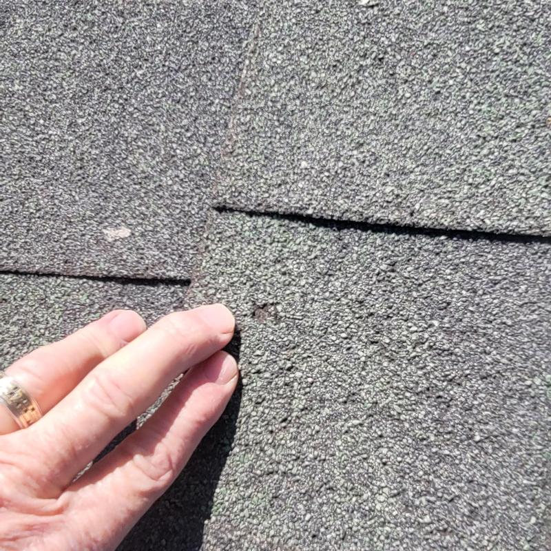 Asphalt roof shingle hail damage close-up with hand