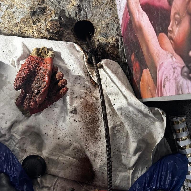 Drain cleaning snake inside floor drain hole with gloves nearby