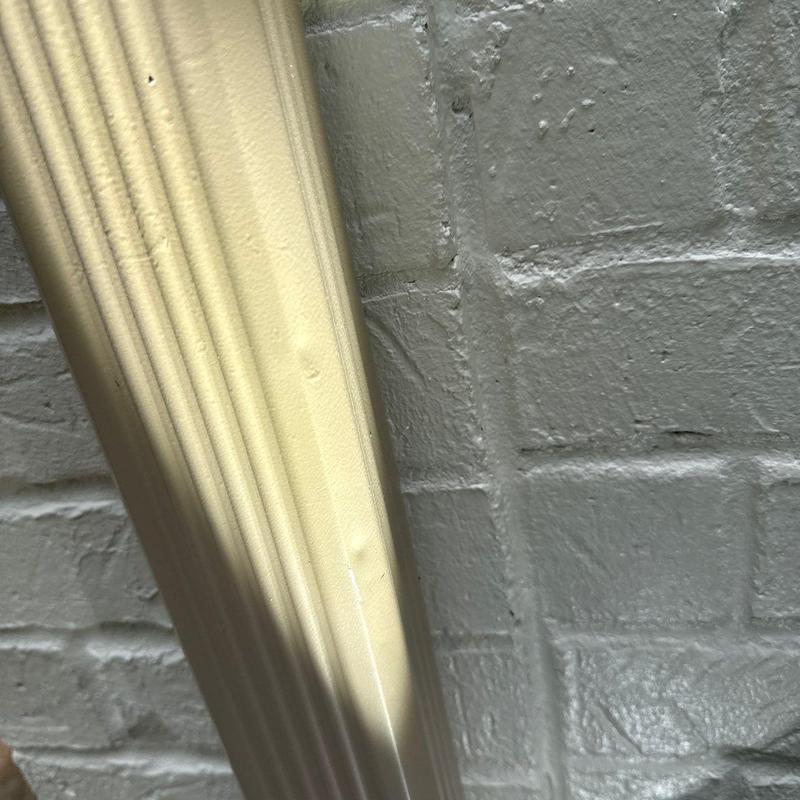 Downspout pipe with dents against brick wall