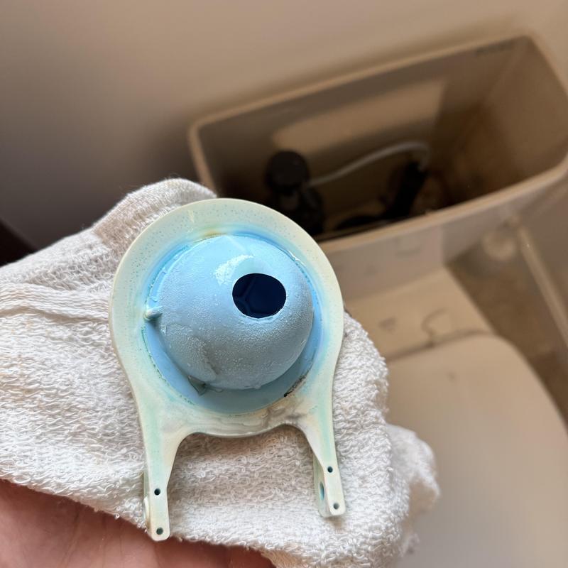 Toilet flapper valve held over open tank with white towel