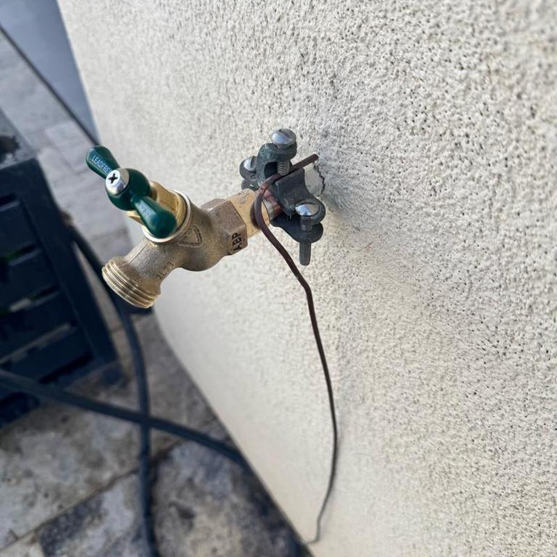 Hose bib with grounding wire attached to stucco wall