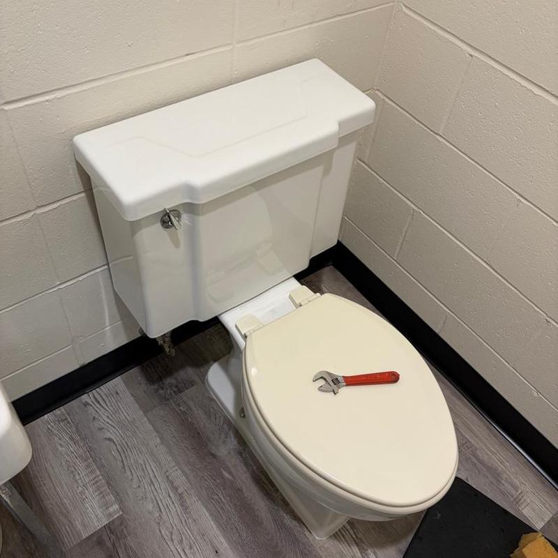 Toilet with wrench on seat in bathroom corner