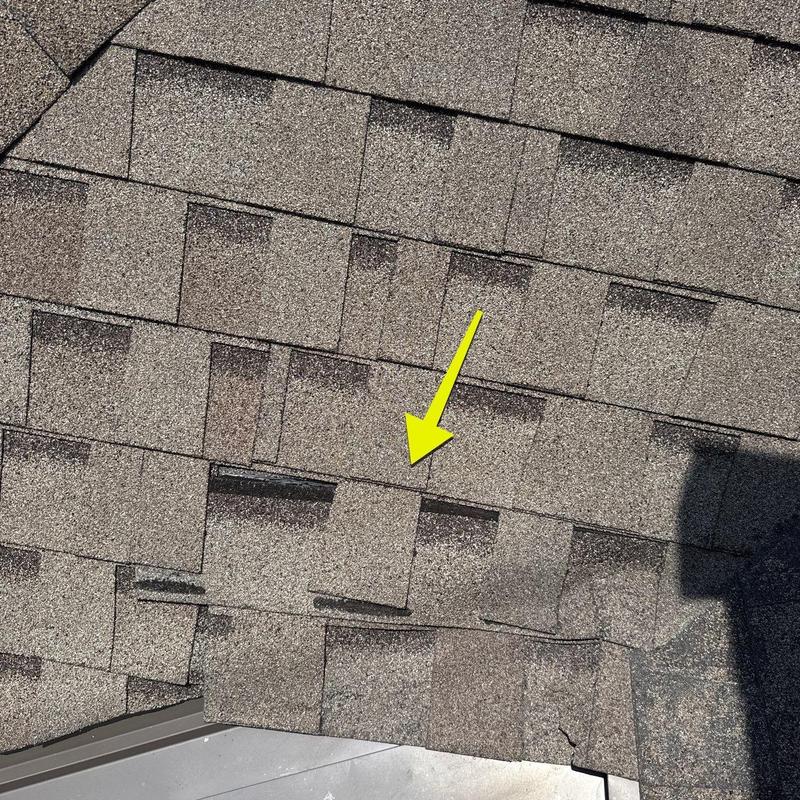 Asphalt roof shingles with hail damage marked by arrow