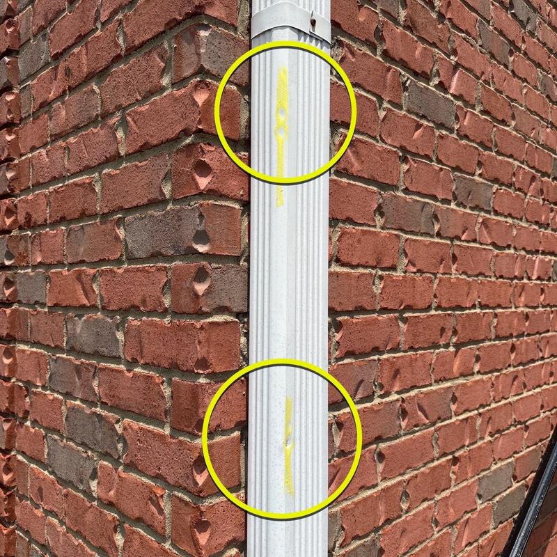 Downspout with visible dents and paint damage on brick wall