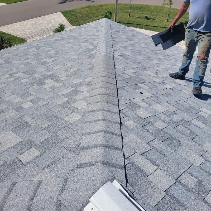 Hip cap shingles on gray shingle roof with worker nearby