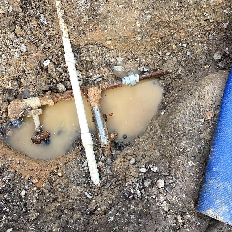 Rusty underground plumbing pipes with water leak in soil