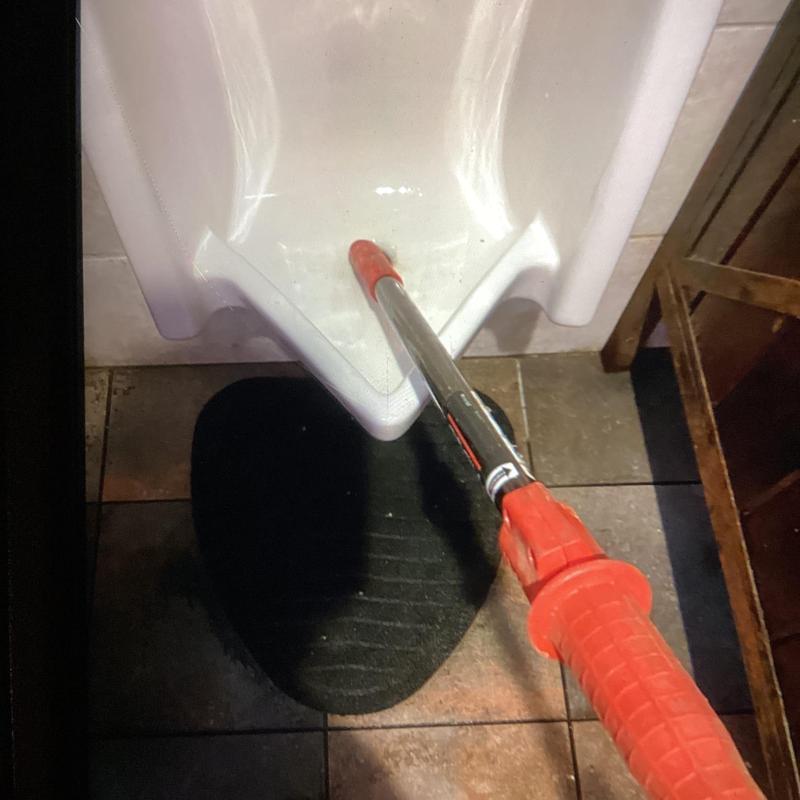 Urinal blockage clearing with plumbing tool in restroom