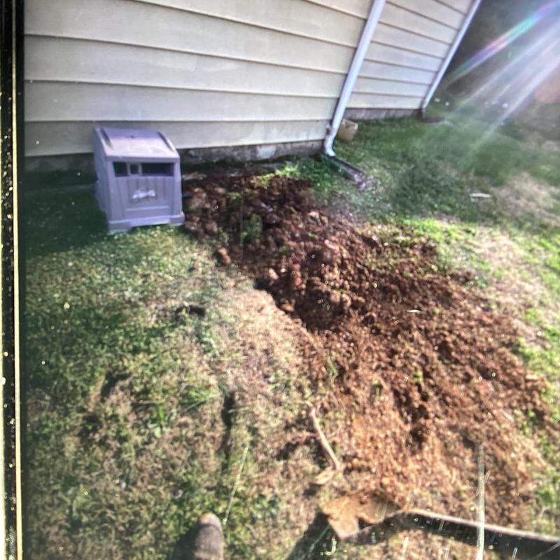 Sewer line excavation beside house siding with soil mound