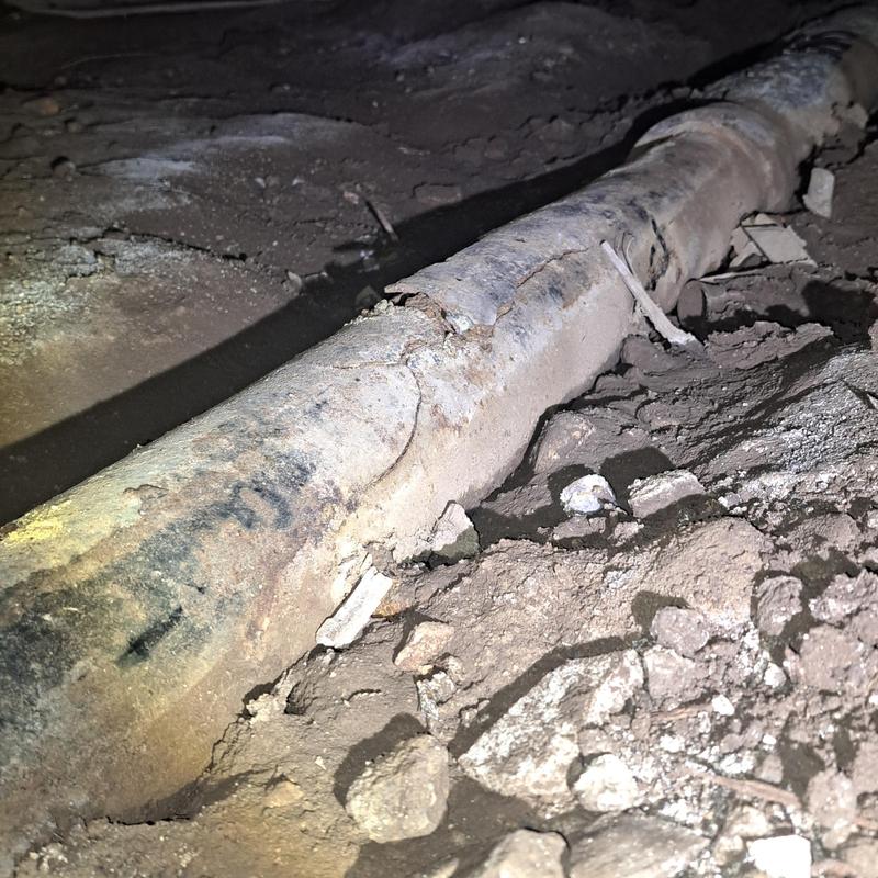 Cast iron drain pipe with corrosion damage under house dirt