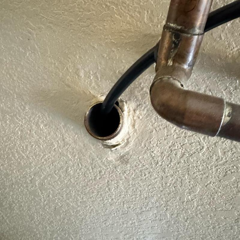 Copper plumbing pipes entering ceiling hole with black cable