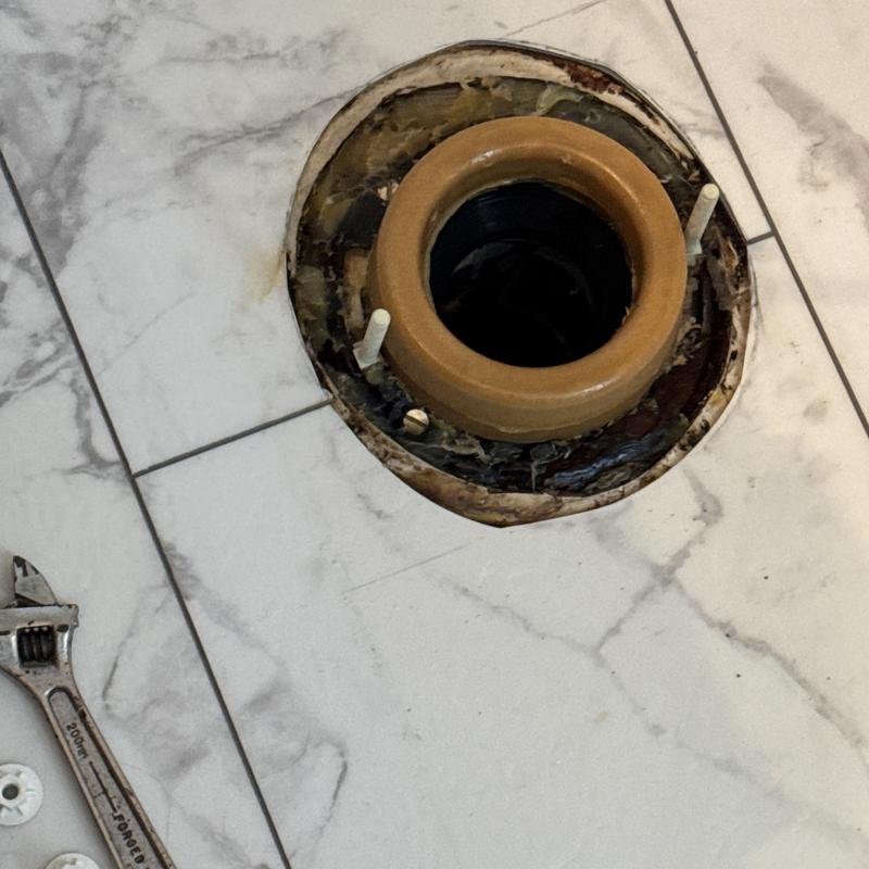 Toilet flange on marble floor with wrench nearby