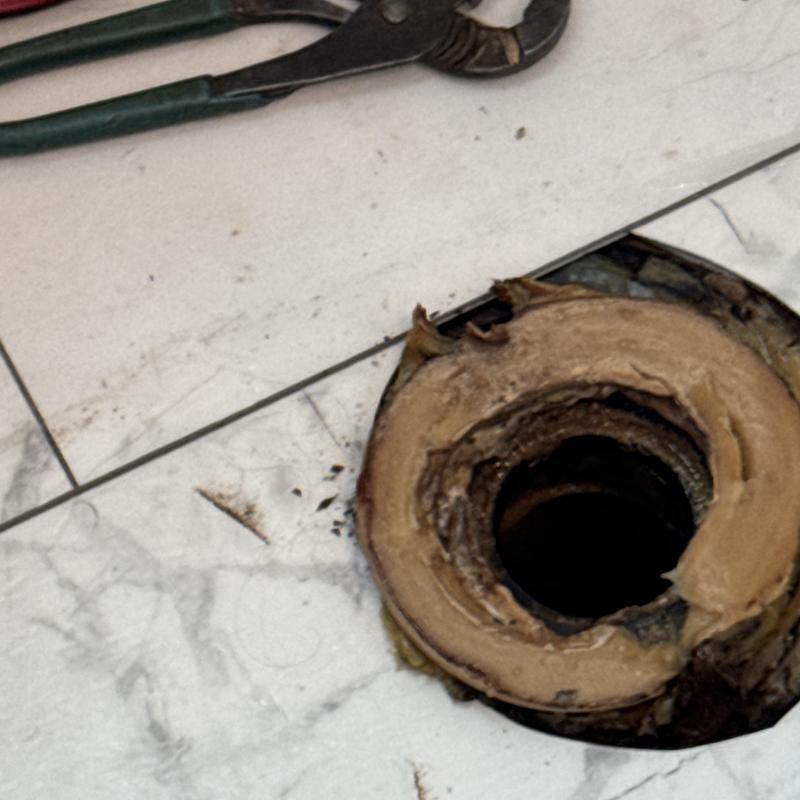 Toilet flange with wax ring removed on tiled floor