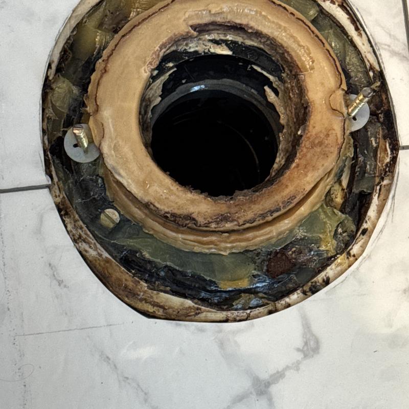 Toilet flange with corrosion and damaged seal on marble floor