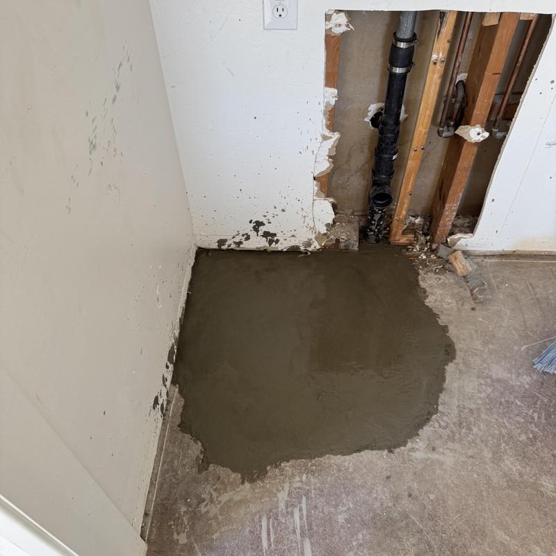 Drain pipe area concrete floor patching near wall studs