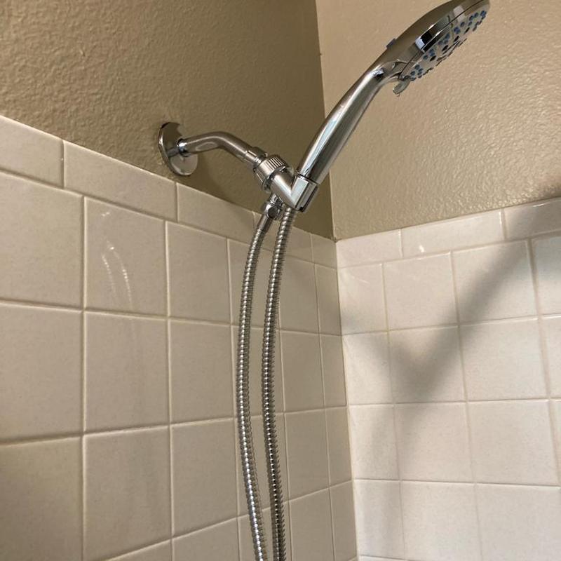 Handheld shower head and chrome arm on tiled wall