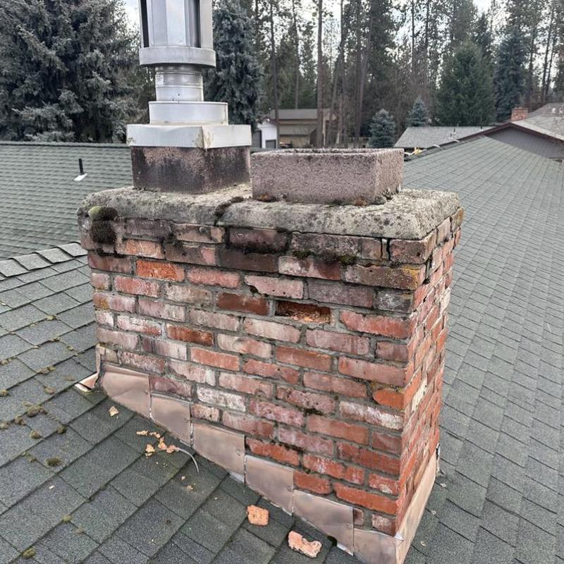 Brick chimney with mortar damage on roof shingles