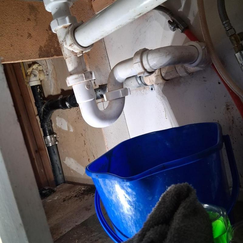 Kitchen sink drain pipes with blue bucket and cleaning rag