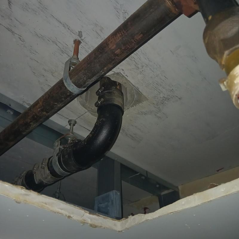 Black drain pipe with metal clamps in ceiling space