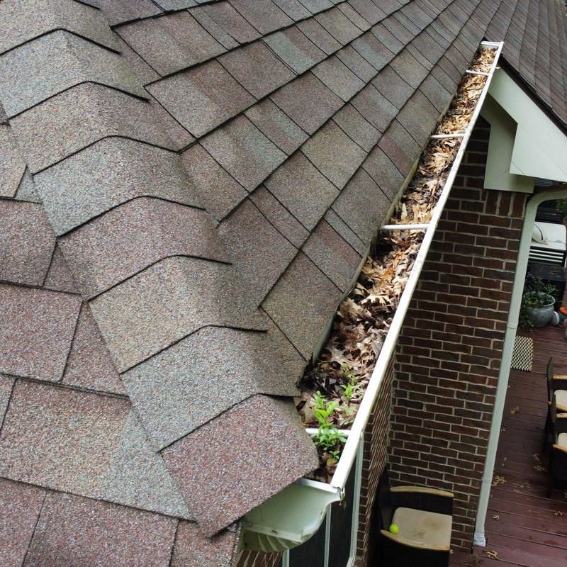 Asphalt shingle roof with debris-filled gutter and slight damage